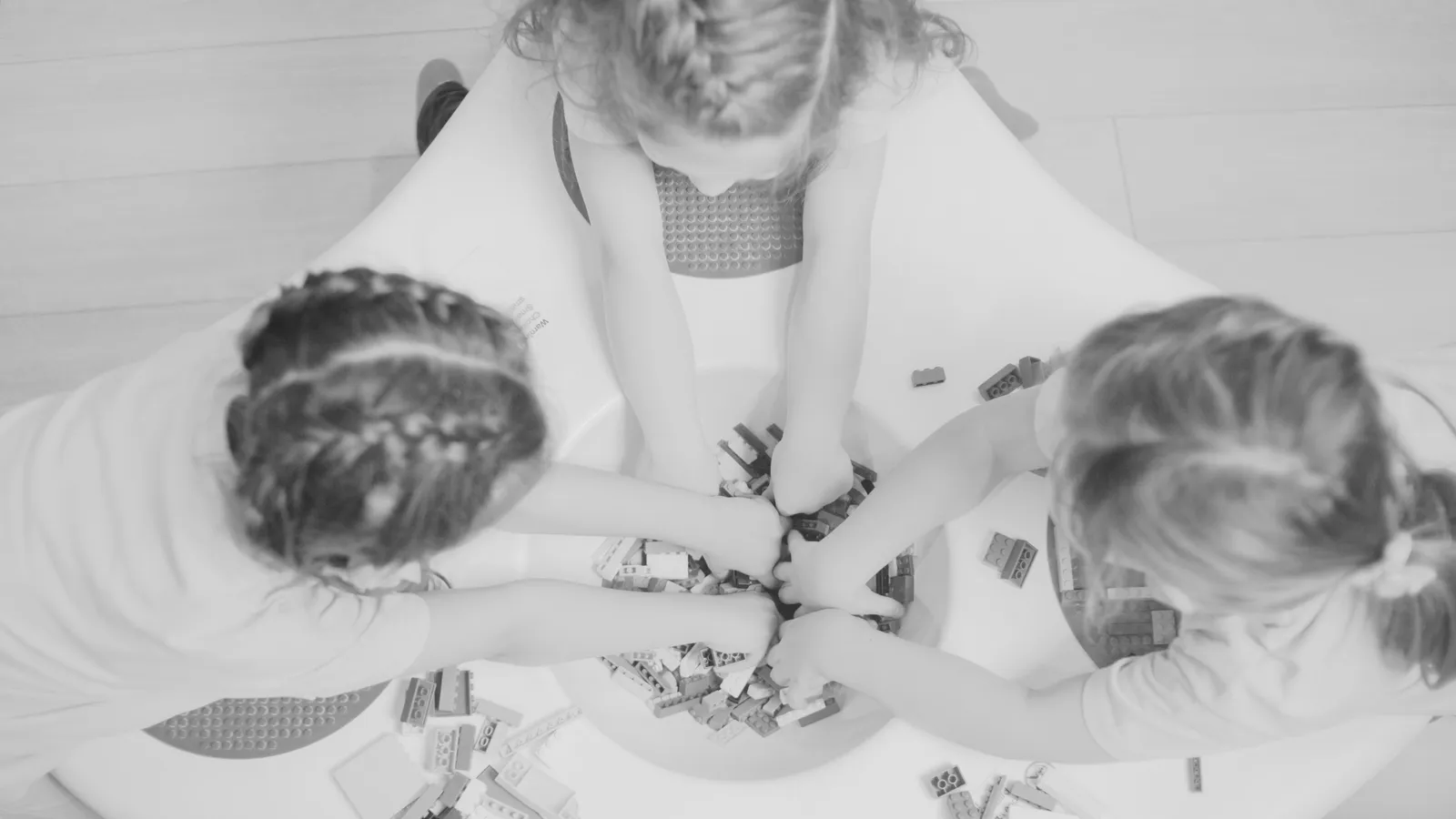 Three children playing with Legos at a round white table.