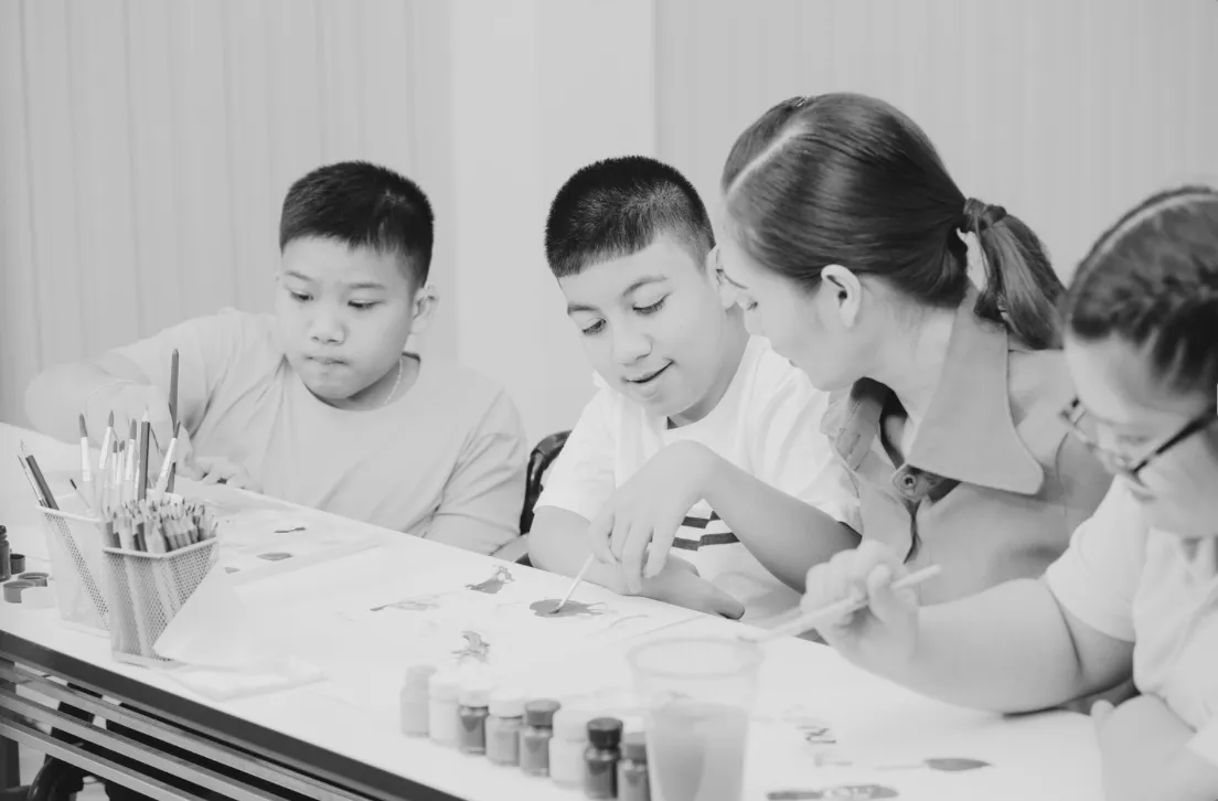 Children and a teacher sitting at a table, engaging in an art activity with paints and brushes.