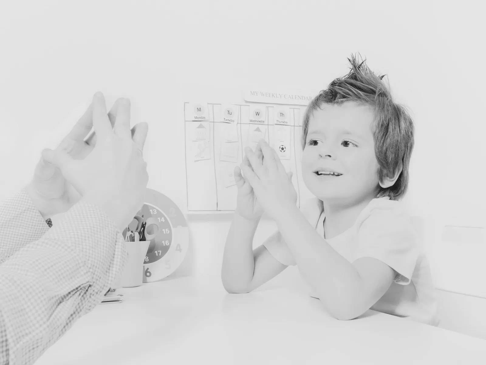 Child and adult giving a high five in a classroom, with a weekly calendar and clock in the background.