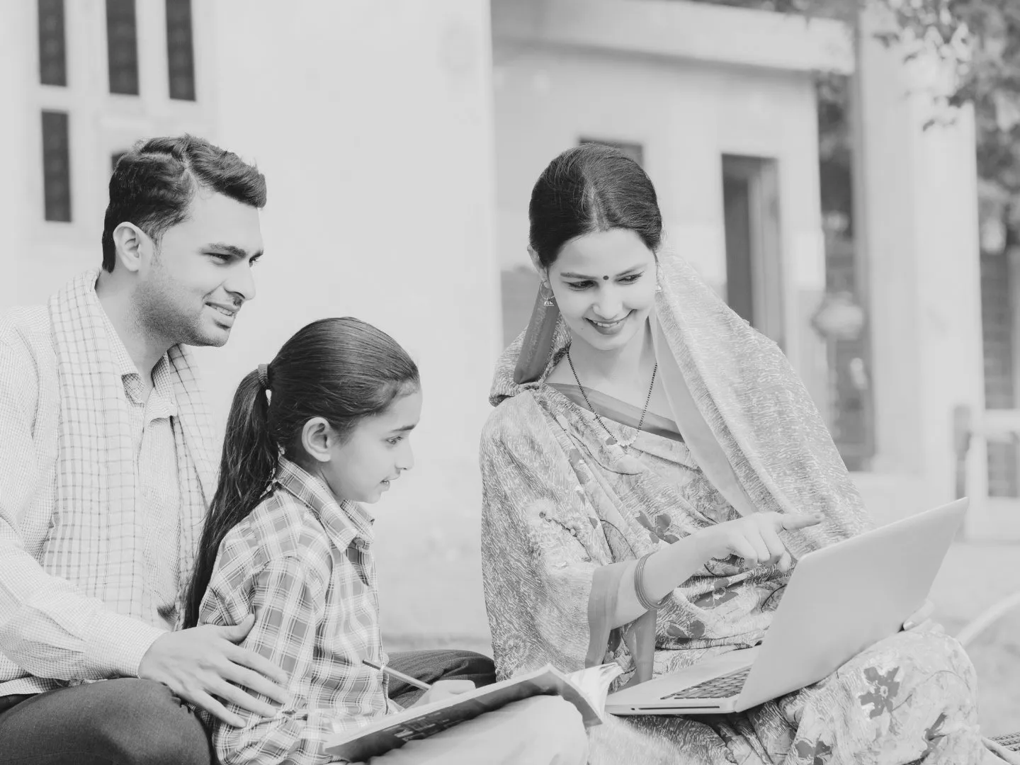 A family of three and a woman, all looking at a laptop outdoors.